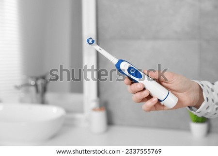 Woman holding electric toothbrush in bathroom at home, closeup