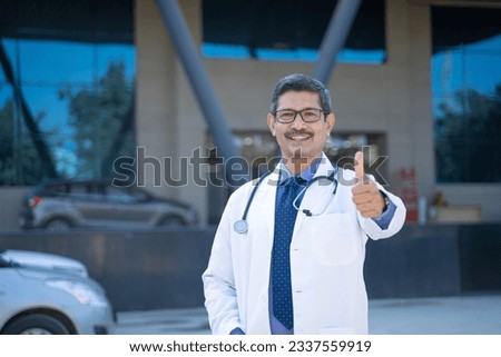 Doctor standing in front of hospital and showing thumps up Royalty-Free Stock Photo #2337559919