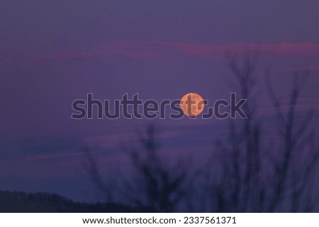 Mystical landscape with full moon rise in the cold season. The natural satellite of the earth observed at sunset among the colored clouds
