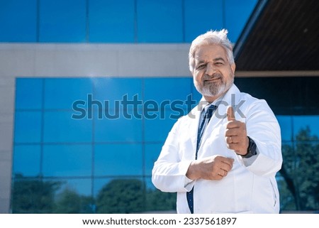 Senior doctor standing in front of hospital and showing thumps up