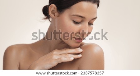 Beauty and skincare portrait with copy space for text. Crop photo of the woman with a beautiful young adult face touching her shoulder. A tender Asian girl with natural makeup enjoys glowing hydrated