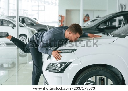 Kissing the new automobile. Handsome car dealership worker is with electric vehicle. Royalty-Free Stock Photo #2337579893