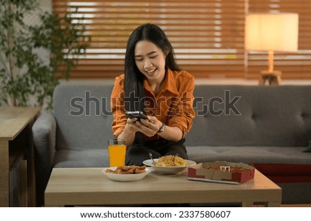 Smiling teenager girl using smartphone for taking a photo of her meal while sitting in cozy living room
