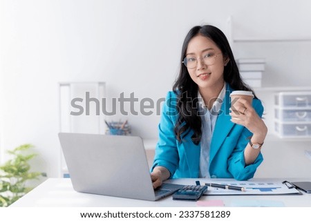 Successful Asian businesswoman smiling using laptop computer and holding coffee cup at office. Confident Asia businesswoman sitting happily in the office.