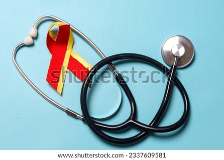 Stethoscope with red yellow ribbon over blue background, symbolic bow color to support patient with illness and hepatic disease. World hepatitis day, HIV HVC co-infection