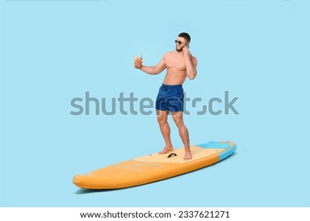 Happy man with refreshing drink talking on smartphone on SUP board against light blue background