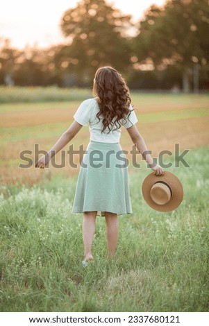 Beautiful young Asian woman in field at sunset. Model with dark long curly hair. Summer, sun.