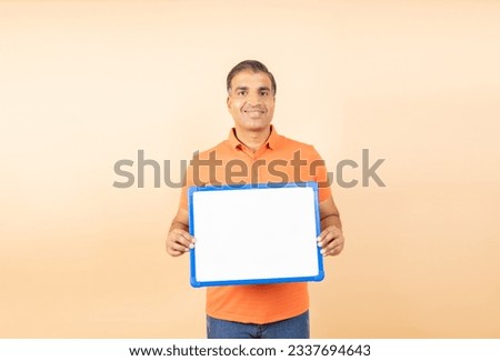 Happy indian man holding blank place card to put message isolated on beige background. Signboard Promotion and Advertisement concept.