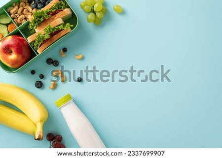 Wholesome lunchtime concept portrayed from a top-down view. The lunchbox holds nutritious sandwiches, fruits, buts and berries on blue isolated background, offering copyspace for text or promotions Royalty-Free Stock Photo #2337699907