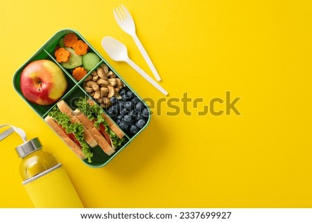 Organic school lunch presentation. Top view exhibiting eco-conscious lunchbox filled with nutritious treats, fruits, veggies, berries, nuts, water bottle, cutlery on yellow surface with room for ad