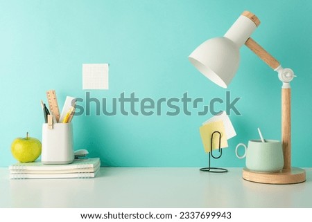Foster a focused study environment with this side-view picture of white desktop with school supplies, penholder and desk lamp on a blue isolated background, designed for easy text or ad placement