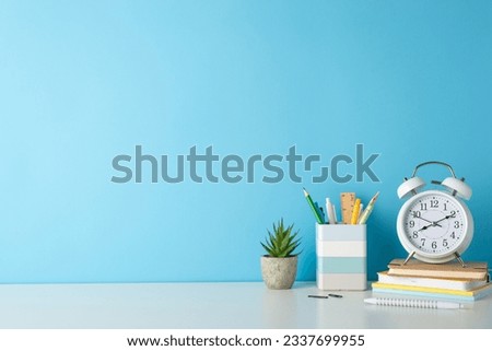 Promote a productive study environment with side-angle photo featuring white desk, alarm clock, notepads, penholder, and office supplies on blue backdrop, providing ample copy-space for text or ads Royalty-Free Stock Photo #2337699955