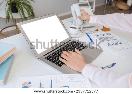 Woman working on laptop at white table with different charts and phone