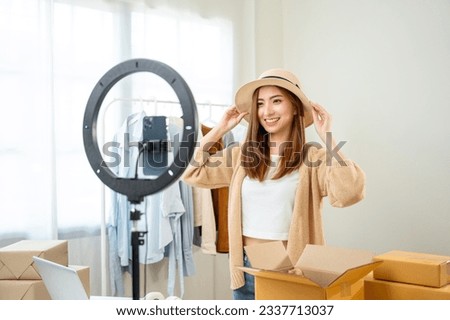 Young asian woman business owner at fashion store using cellphone live streaming for sale fashion hat and clothing. Influencers record video review item for sell on social media. Online shopping Royalty-Free Stock Photo #2337713037
