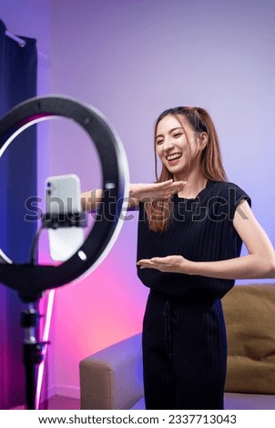 Young trendy influencer asian woman dancing on mobile phone at home in living room with neon light. Creator vlogger talent dancing enjoy hobby content recording show video sharing on social media. Royalty-Free Stock Photo #2337713043