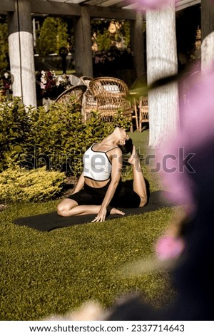 A fit, pretty woman in sports clothes meditates while sitting in a lotus position on the green grass near her house. young woman doing yoga exercises at home outdoors 