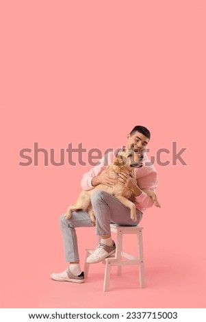 Young man with cute Labrador dog sitting on stepladder against pink background