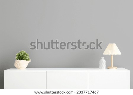 Wooden chest of drawers with houseplant and lamp near grey wall in room Royalty-Free Stock Photo #2337717467