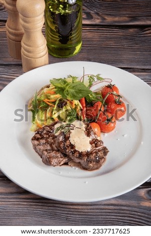 A pieces of steak with salad and pepper sauce. Medium grilled steak with cherry tomatoes and salads