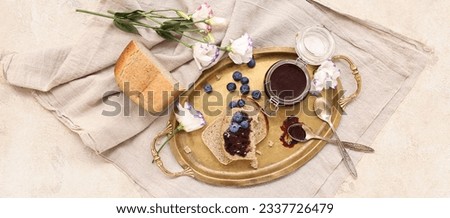 Tray with bread pieces, jar of blueberry jam and flowers on grunge background
