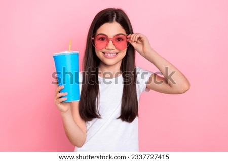 Photo portrait of pretty young child girl hold plastic cup drinking soda dressed stylish white clothes isolated on pink color background