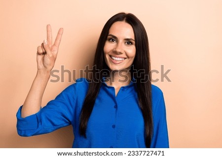 Photo of positive adorable girl wear blue clothes hand showing v-sign symbol good mood isolated on beige color background