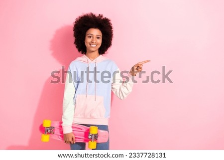 Portrait of cheerful small schoolgirl hand hold skateboard indicate finger empty space promo isolated on pink color background