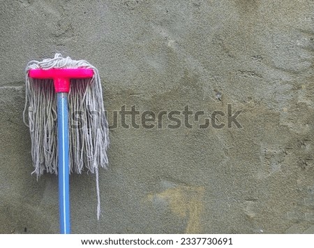 Floor mop leaning on cement concrete wall background with copy space