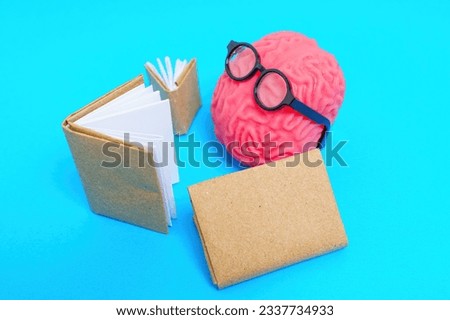 Human brain model adorned with nerdy glasses reading books isolated on blue background.