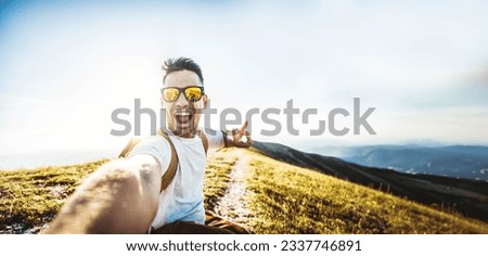 Happy man with backpack and sunglasses taking selfie picture on top of the mountain - Cheerful hiker climbing the cliff outdoors - Travel blogger looking at camera - Pov view