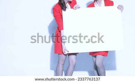 Two women dressed in red holding a white board are showing an introduction gesture at Broad