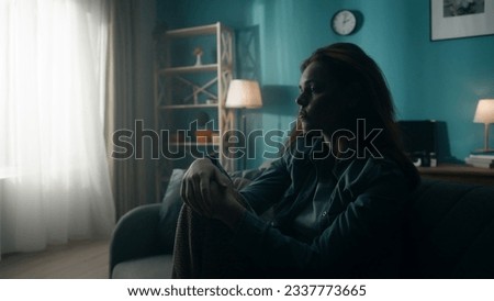 A devastated, lonely young woman sits on a sofa in a dark room close up. A woman desperately thinks about personal problems, experiencing a crisis. Hopelessness. Mental health concept. Royalty-Free Stock Photo #2337773665