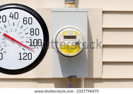 Outdoor thermometer with electric meter in the sun during heatwave. Hot weather, energy savings and utility bill costs concept. Royalty-Free Stock Photo #2337790479