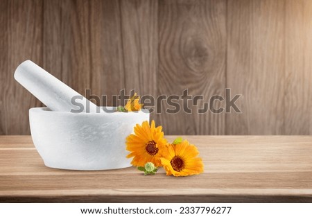 Calendula officinalis flowers in mortar on wood table background. Marigold medicinal plant, herbal medicine, naturopathy and phytotherapy. Ingredient for natural beauty products and cosmetics. 