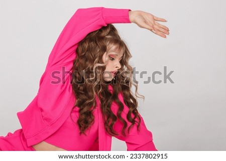 young girl in pink suit poses as doll on white background in studio