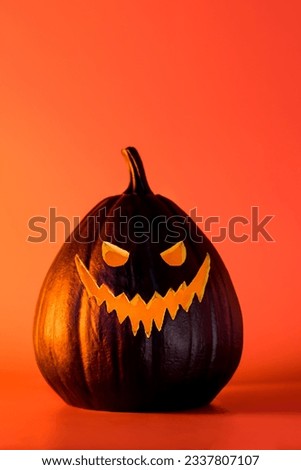 Spooky halloween black pumpkin, Jack O Lantern, with illuminated evil face and eyes on bright orange background with copy space. Happy Halloween decor concept. Festive vertical postcard.