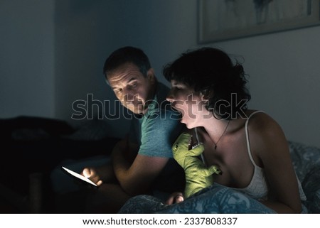 Dad and daughter are sitting on bed in teenage room, with smartphones, daughter screams, expresses displeasure, emotionally closing eyes, at night. Generation conflict, dad and daughter quarrel.