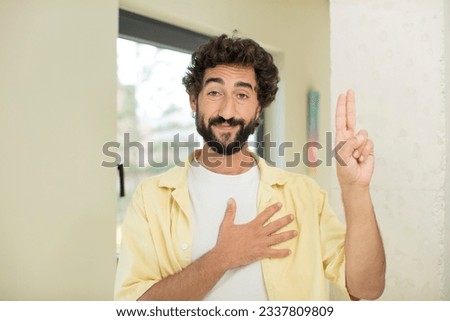 young crazy bearded man looking happy, confident and trustworthy, smiling and showing victory sign, with a positive attitude
