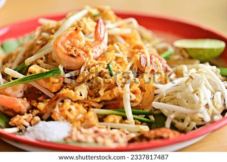 Pad Thai is placed on a brown wooden table. There is a woman squeezing lime juice to add more seasoning. Because Thai people like to eat spicy food. Famous Thai food concept. Street food. Thai identit