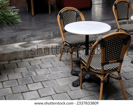 Empty comfortable vintage rattan chair seats with round marble table decorated on grey concrete brick tile floor inside the natural dim light building with copy space. Cozy living zone interior.