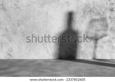 Shadows from a bottle of wine and a glass on a gray concrete background. Minimalist mockup with shadows and lights.