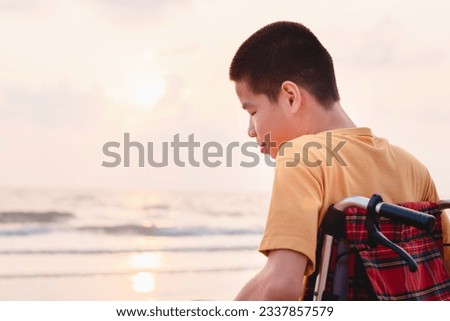 Asian boy with happy face on the sunset sea beach, Beautiful moment nature,Traveling using a wheelchair to learn about the world without limits with support from family,Good mental health,positive pic