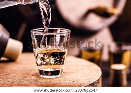 Glass of golden rum, with bottle. Bottle pouring alcohol into a small glass. Brazilian export type drink. Brazilian product for export, distilled drink known as brandy or pinga. Day of cachaça. Royalty-Free Stock Photo #2337862547