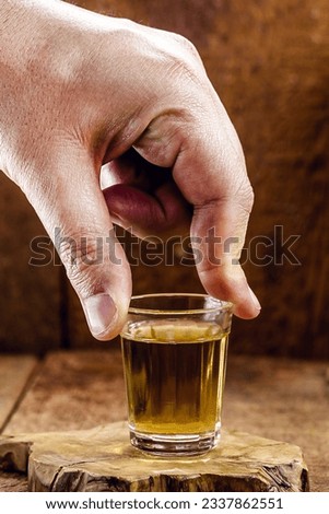 male hand holding a glass of distilled alcoholic beverage, called "pinga" or "cachaça" in Brazil, scenery of alembic Royalty-Free Stock Photo #2337862551