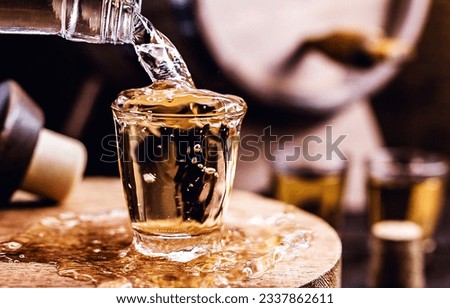 Glass of golden rum, with bottle. Bottle pouring alcohol into a small glass. Brazilian export type drink. Brazilian product for export, distilled drink known as brandy or pinga. Day of cachaça. Royalty-Free Stock Photo #2337862611