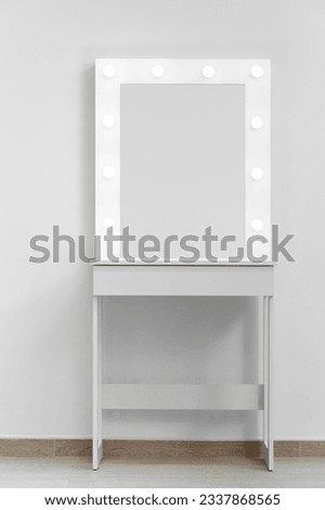 A white makeup dressing table with a large mirror and lights on against the wall. Makeup artist's workplace, modern dressing room. Royalty-Free Stock Photo #2337868565
