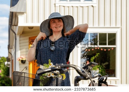 Smiling woman in a vintage dress and gray hat staying by her electric bicycle on a town street. Selective focus
