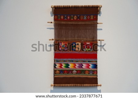 Striped Hand Woven Vintage kilim or rug hanging on a wooden hanger against white wall