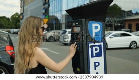 Woman in sunglasses and dress type registration plate number on parking meter. Elegant generation z female driver press keypad buttons on parking kiosk to buy parking ticket.