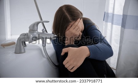 Upset crying woman sitting in bath after being victim of abuse or violence. Royalty-Free Stock Photo #2337918771